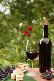 Photo of Red wine, cheese, nuts and grapes on wooden table outdoors, space for text