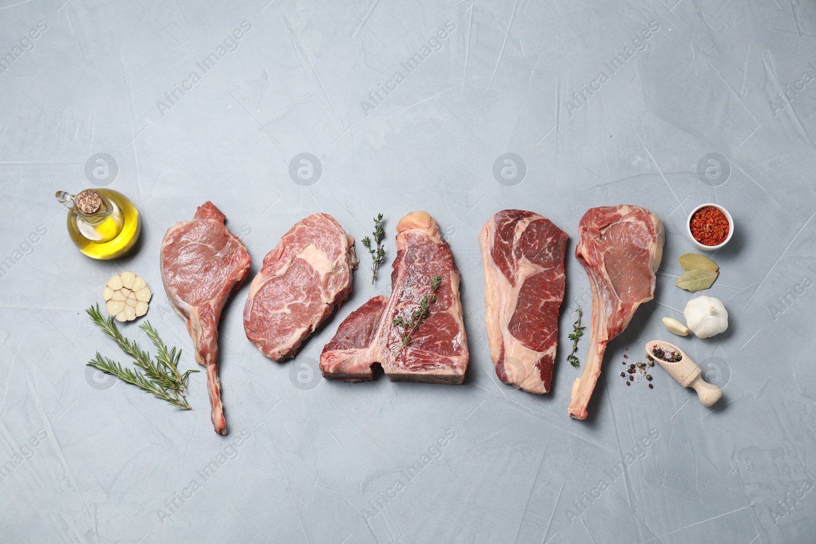 Photo of Fresh raw beef cuts, spices and oil on light grey textured table, flat lay