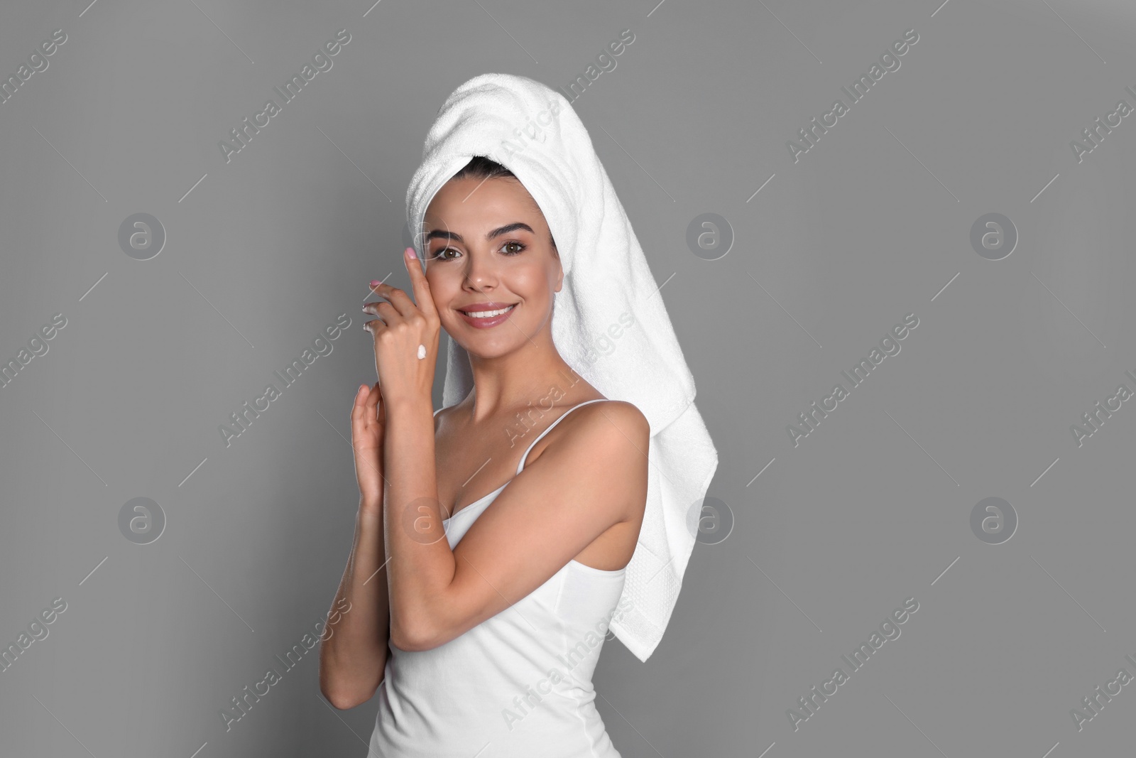 Photo of Beautiful young woman with towel applying cream on hand against grey background