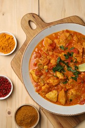 Delicious chicken curry and spices on wooden table, flat lay