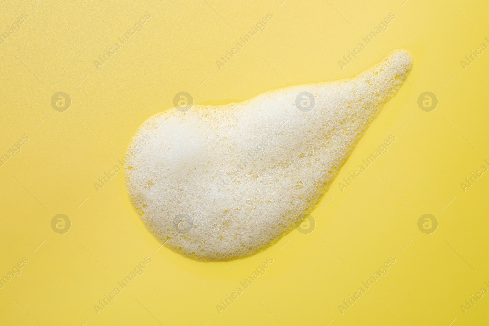 Photo of Drop of fluffy soap foam on yellow background, top view