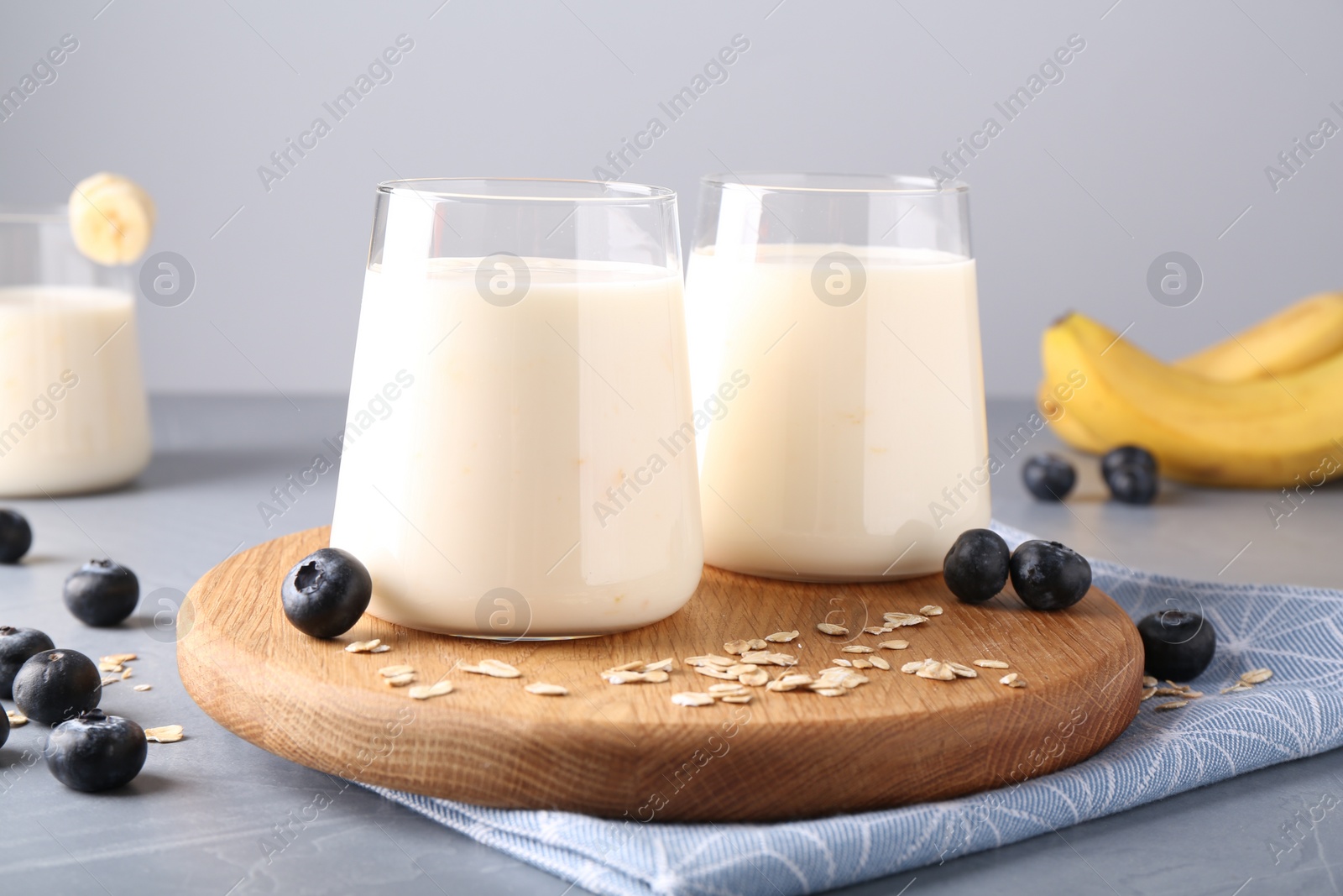 Photo of Tasty yogurt in glasses, oats and blueberries on grey table