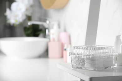 Photo of Container with cotton swabs and pads on white shelf in bathroom. Space for text