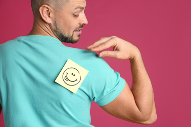 Photo of Man with smiling face sticker on back against pink background. April fool's day