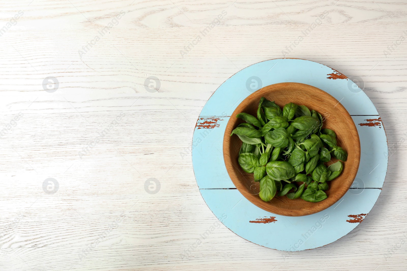 Photo of Fresh green basil leaves in bowl and board on wooden background, top view with space for text