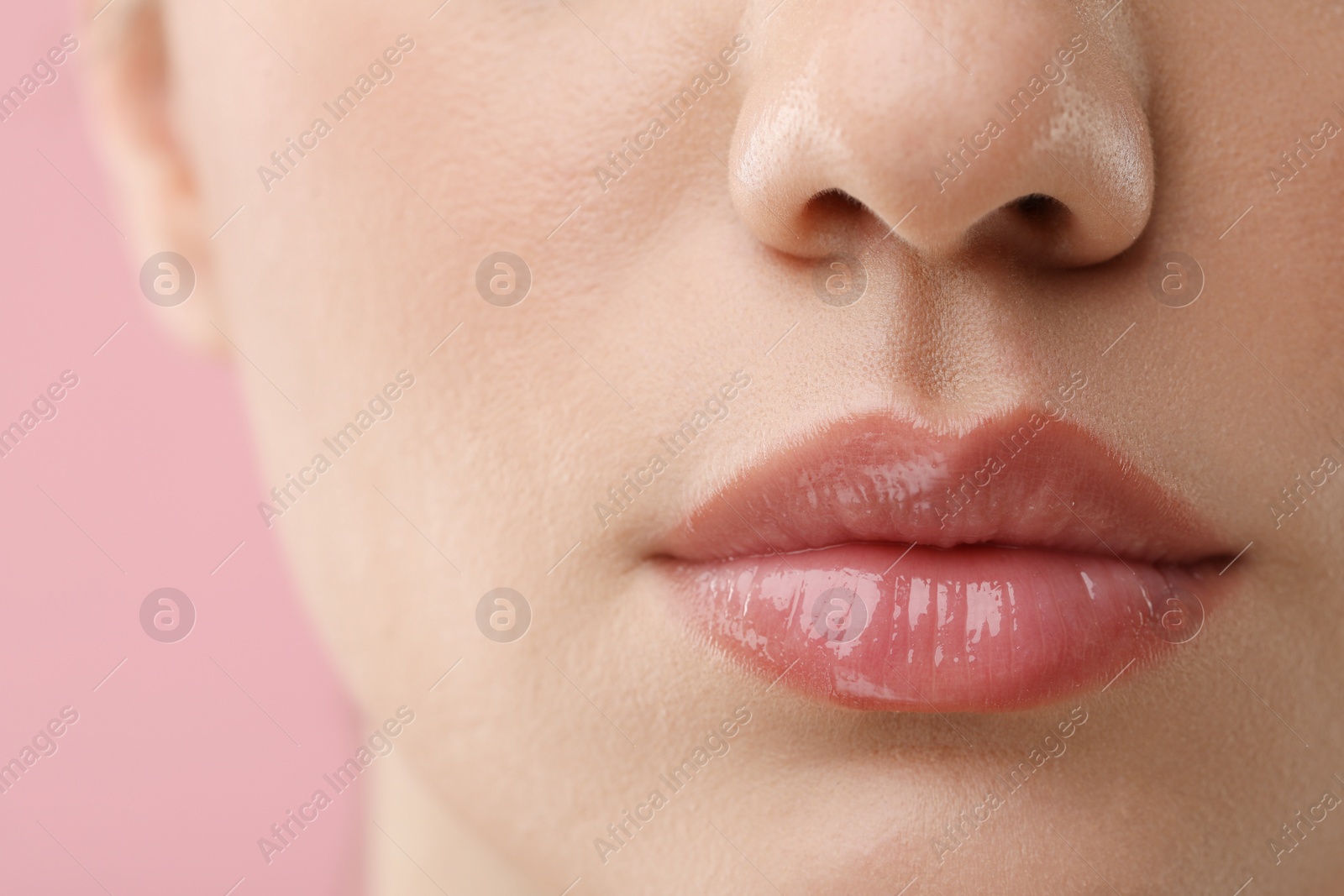 Photo of Woman wearing beautiful lip gloss on pink background, closeup