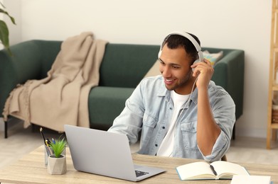 Photo of African American man in headphones working on laptop at wooden table in room