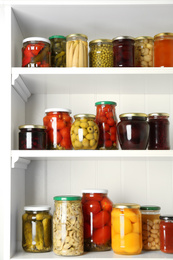 Jars of pickled fruits and vegetables on white wooden shelves