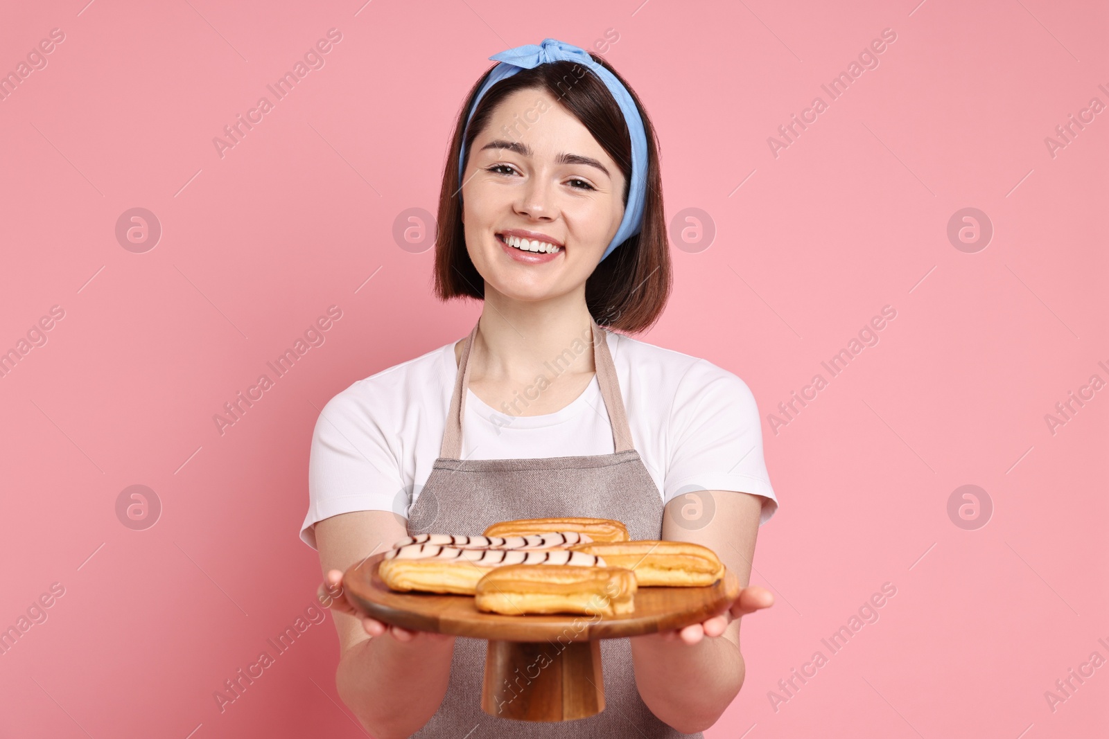 Photo of Happy confectioner with delicious eclairs on pink background