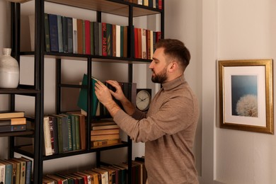 Photo of Young man choosing book on shelf in home library