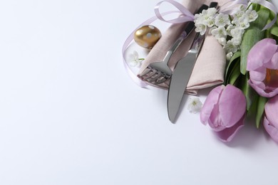 Photo of Cutlery set, Easter egg and beautiful flowers on white background, space for text. Festive table setting