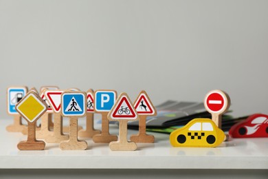 Photo of Wooden road signs and cars on white table near light grey wall, space for text. Children's toys