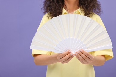Woman holding hand fan on purple background, closeup. Space for text