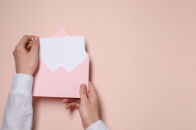 Woman taking card out of letter envelope at beige table, top view. Space for text