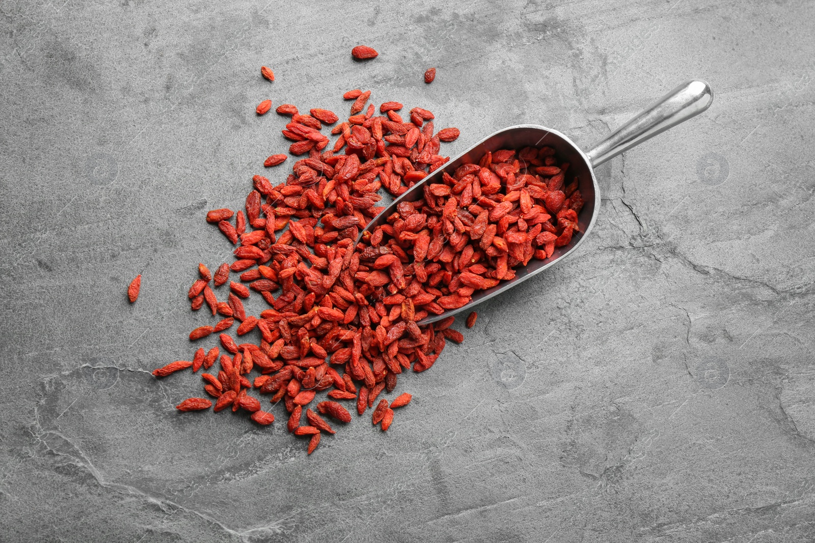 Photo of Scoop and dried goji berries on grey table, top view. Healthy superfood