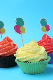 Photo of Delicious cupcakes with bright cream and toppers on light blue background