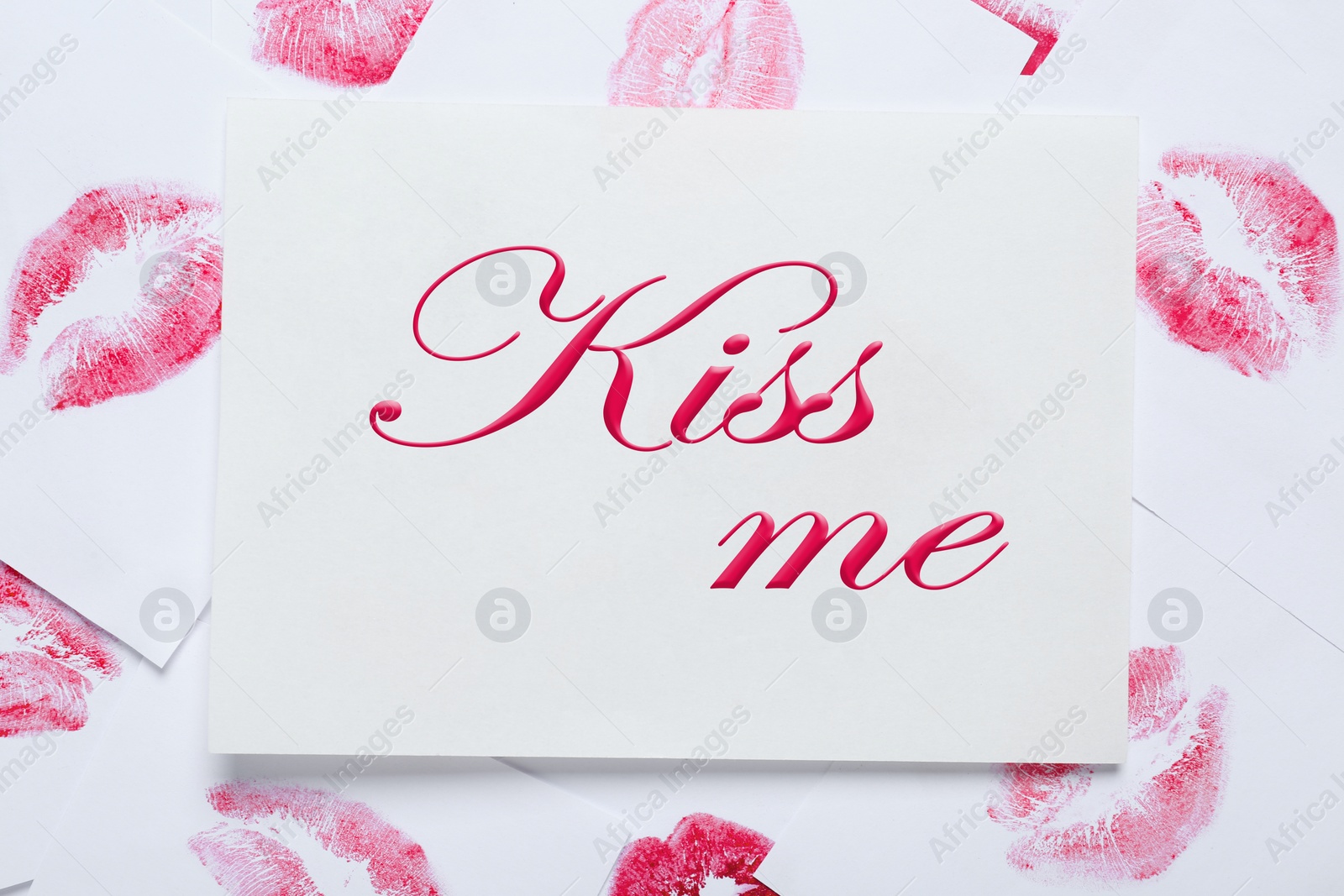 Photo of Card with phrase Kiss Me and lipstick marks on white background, top view