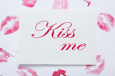 Card with phrase Kiss Me and lipstick marks on white background, top view