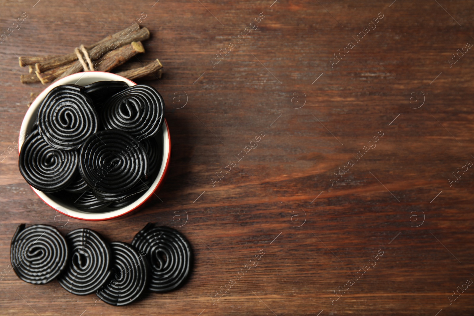 Photo of Tasty black candies and dried sticks of liquorice root on wooden table, flat lay. Space for text