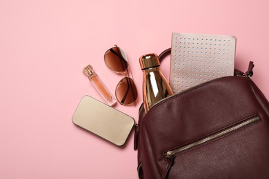 Photo of Stylish urban backpack with different items on light pink background, flat lay