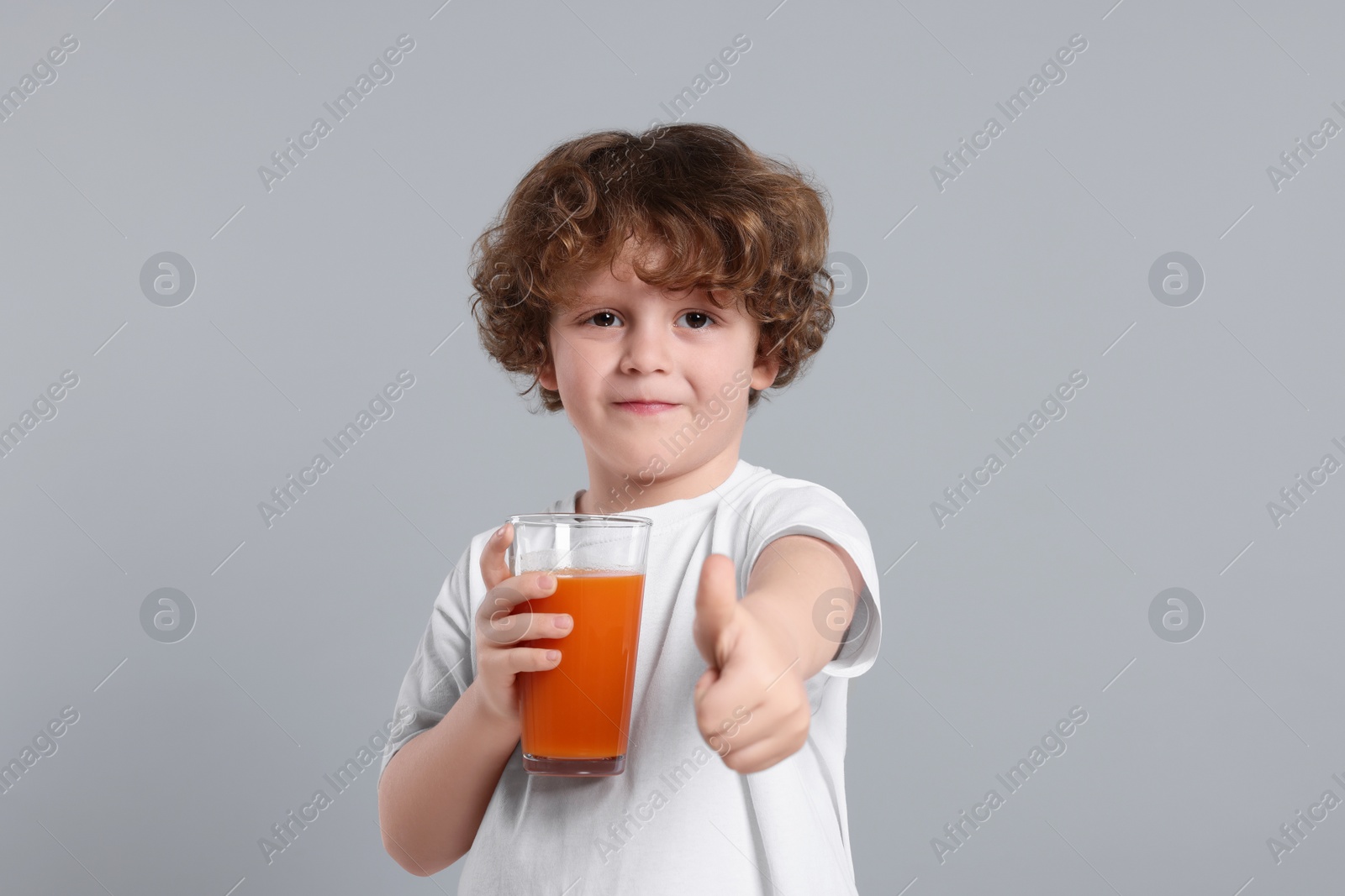 Photo of Cute little boy with glass of fresh juice showing thumb up on light gray background