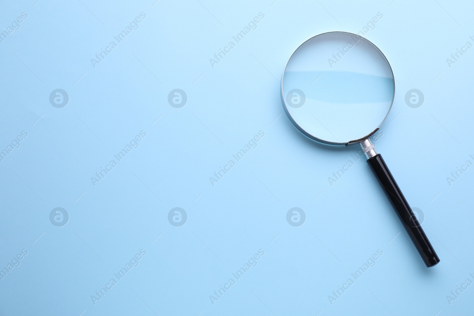 Photo of Magnifying glass on light blue background, top view. Space for text