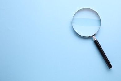 Photo of Magnifying glass on light blue background, top view. Space for text