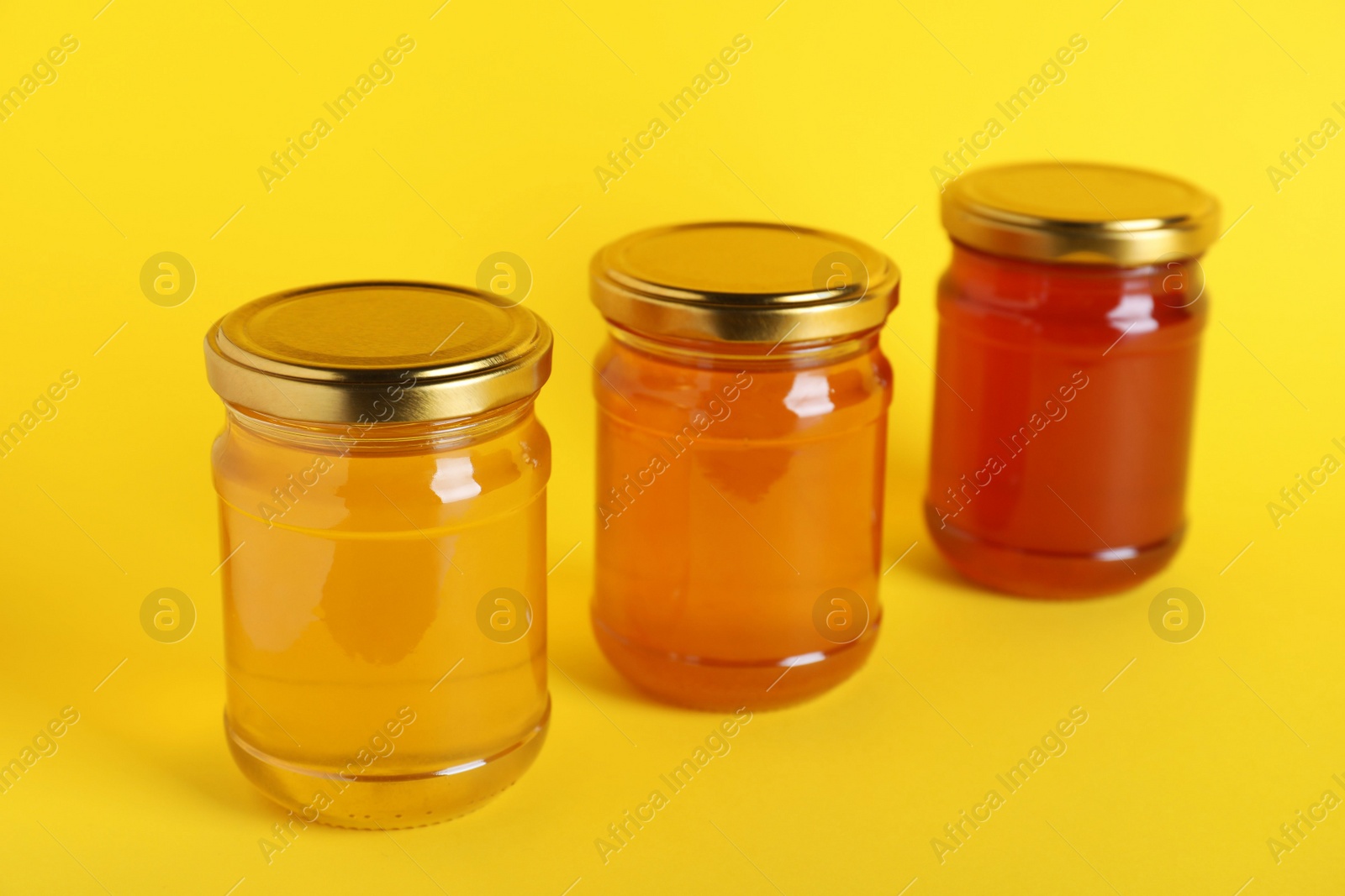 Photo of Jars with different types of organic honey on yellow background