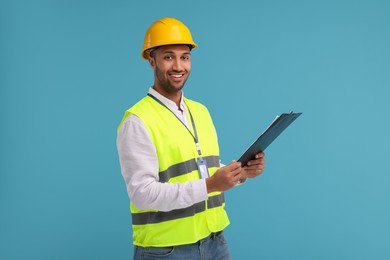 Engineer in hard hat holding clipboard on light blue background