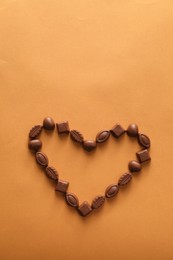 Photo of Heart made with delicious chocolate candies on brown background, top view. Space for text