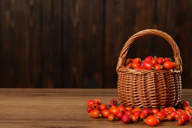 Photo of Ripe rose hip berries with wicker basket on wooden table. Space for text