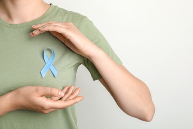 Photo of Woman with blue ribbon on t-shirt against light background. Cancer awareness