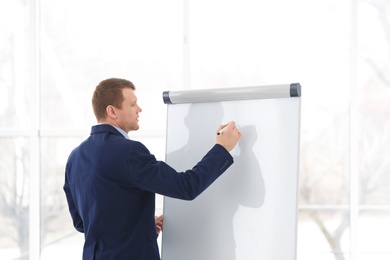 Photo of Business trainer giving presentation on flip chart board indoors