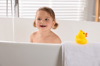 Cute little girl taking bath with toy indoors