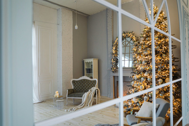 Festive room interior with stylish furniture and beautiful Christmas tree, view through window