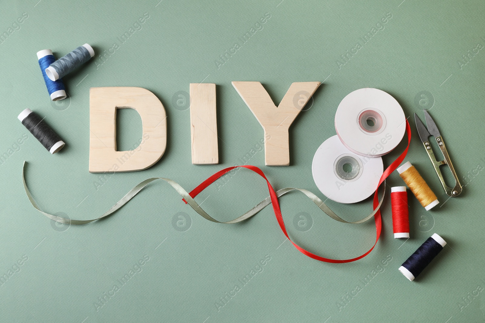 Photo of Abbreviation DIY made of wooden letters and sewing supplies on olive background, flat lay