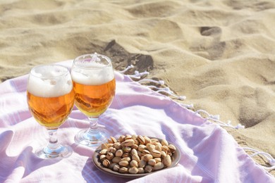 Photo of Glasses of cold beer and pistachios on sandy beach, space for text