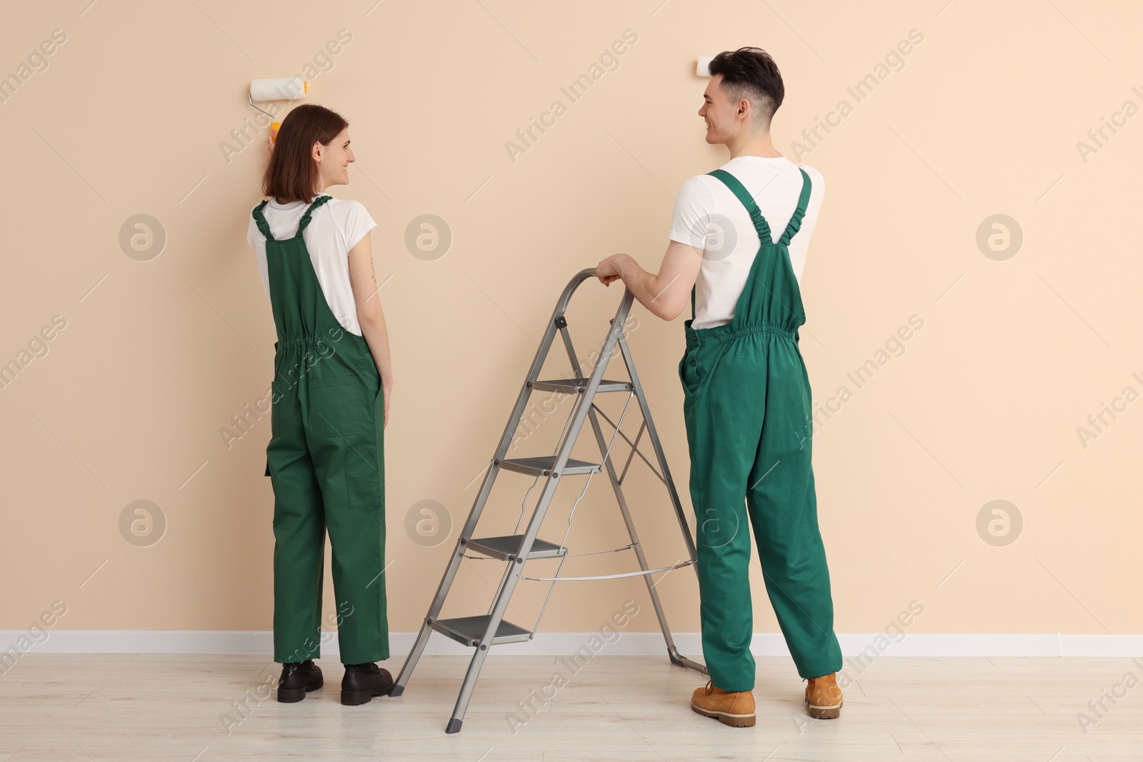 Photo of Young workers painting wall with rollers indoors. Room renovation