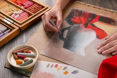 Photo of Woman drawing beautiful jug with soft pastel at wooden table, closeup