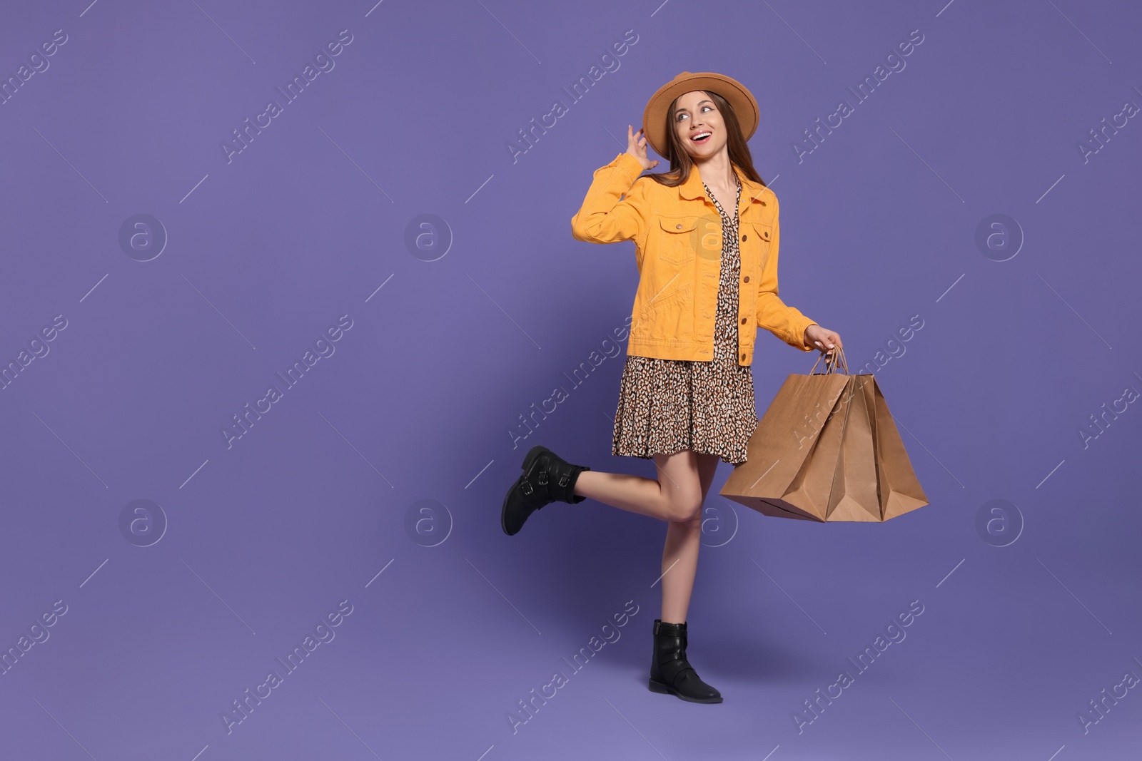 Photo of Stylish young woman with shopping bags on purple background, space for text