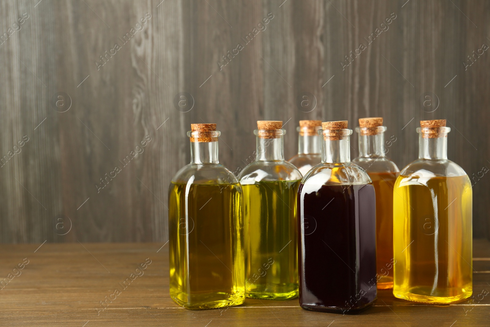 Photo of Vegetable fats. Different oils in glass bottles on wooden table, space for text