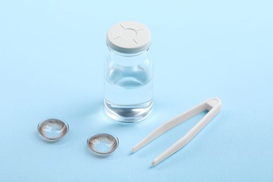 Photo of Color contact lenses, bottle of solution and tweezers on light blue background
