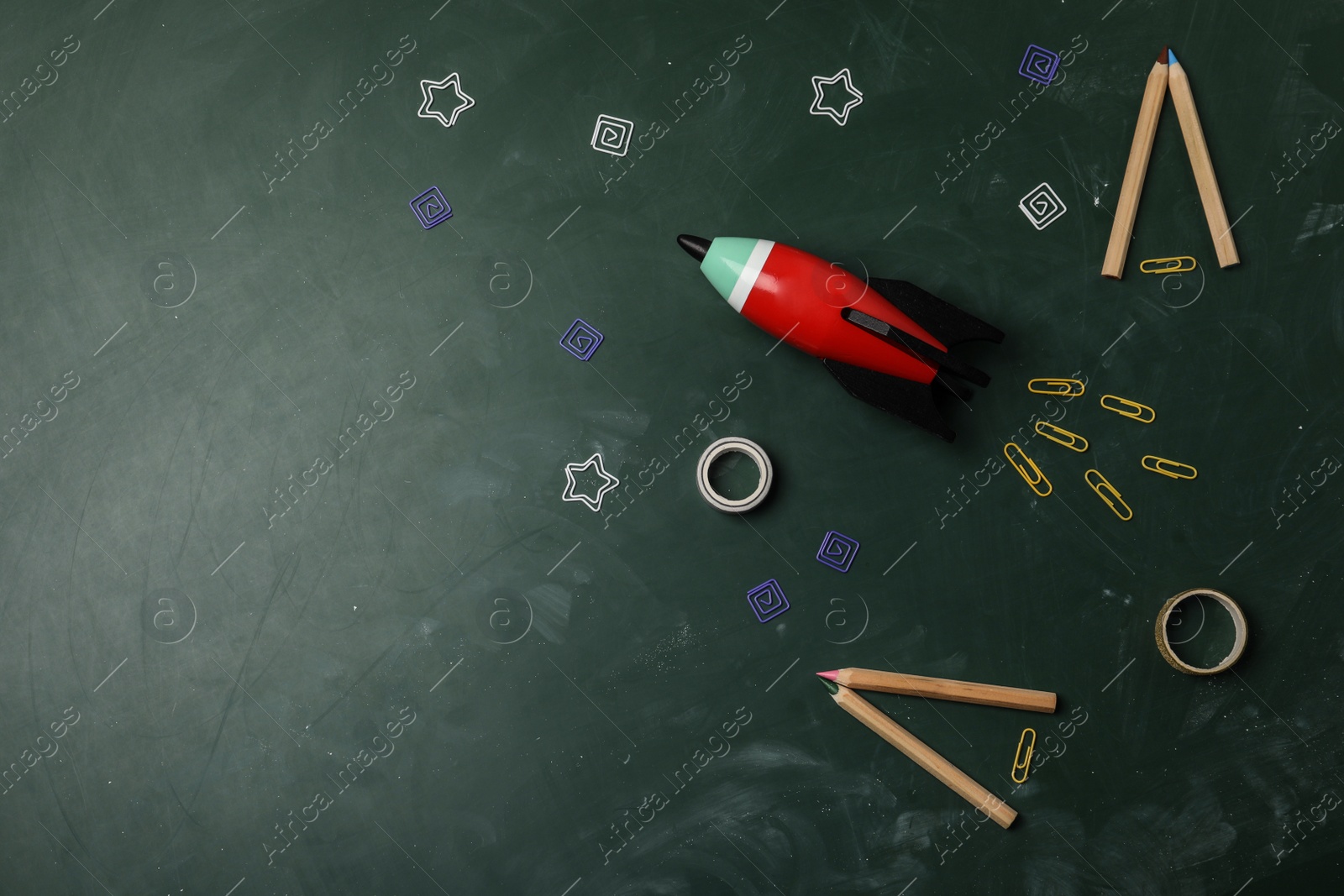 Photo of Bright toy rocket and school supplies on chalkboard, flat lay. Space for text