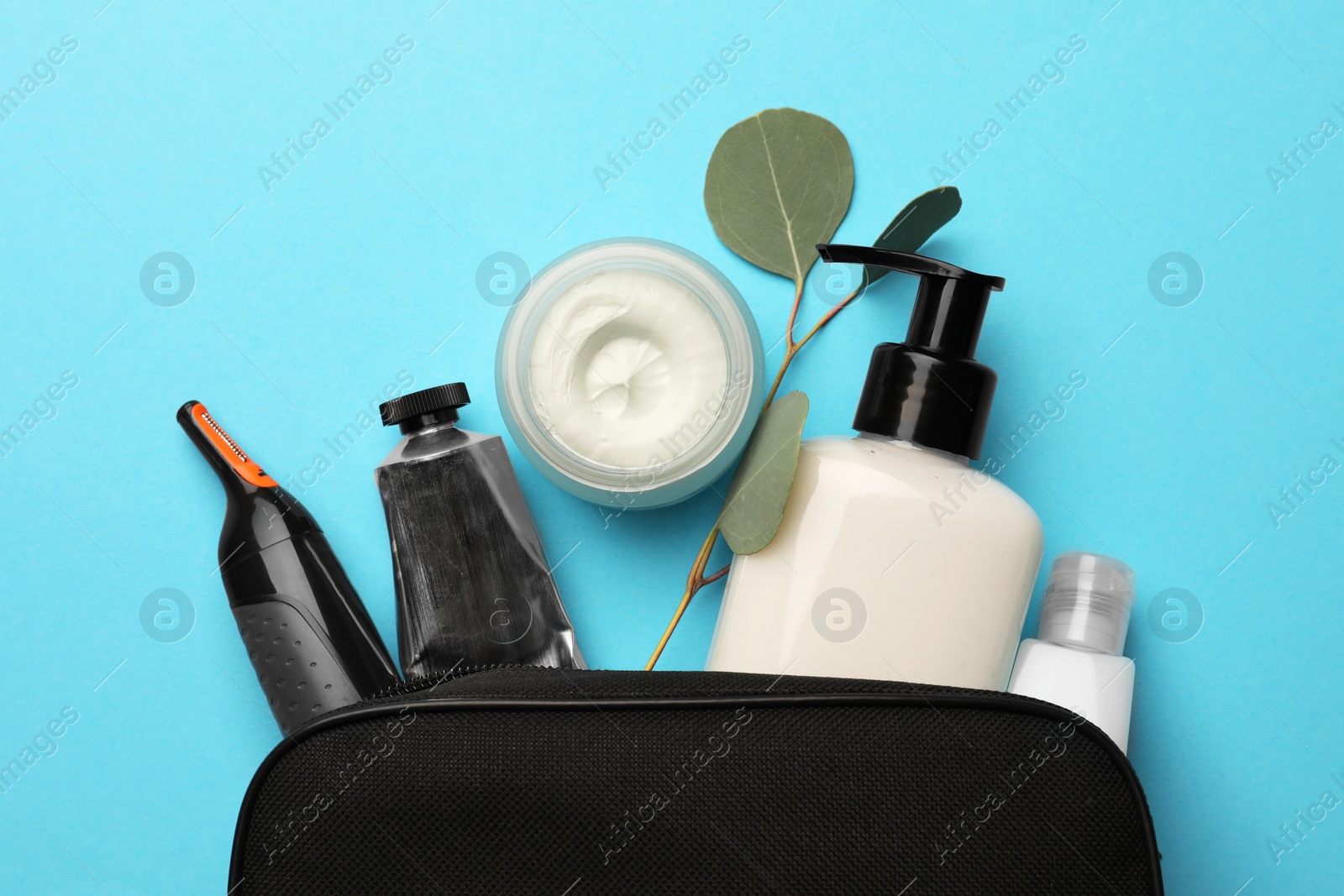 Photo of Preparation for spa. Compact toiletry bag with different cosmetic products and eucalyptus on light blue background, flat lay