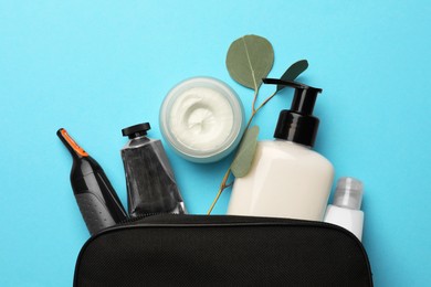 Photo of Preparation for spa. Compact toiletry bag with different cosmetic products and eucalyptus on light blue background, flat lay