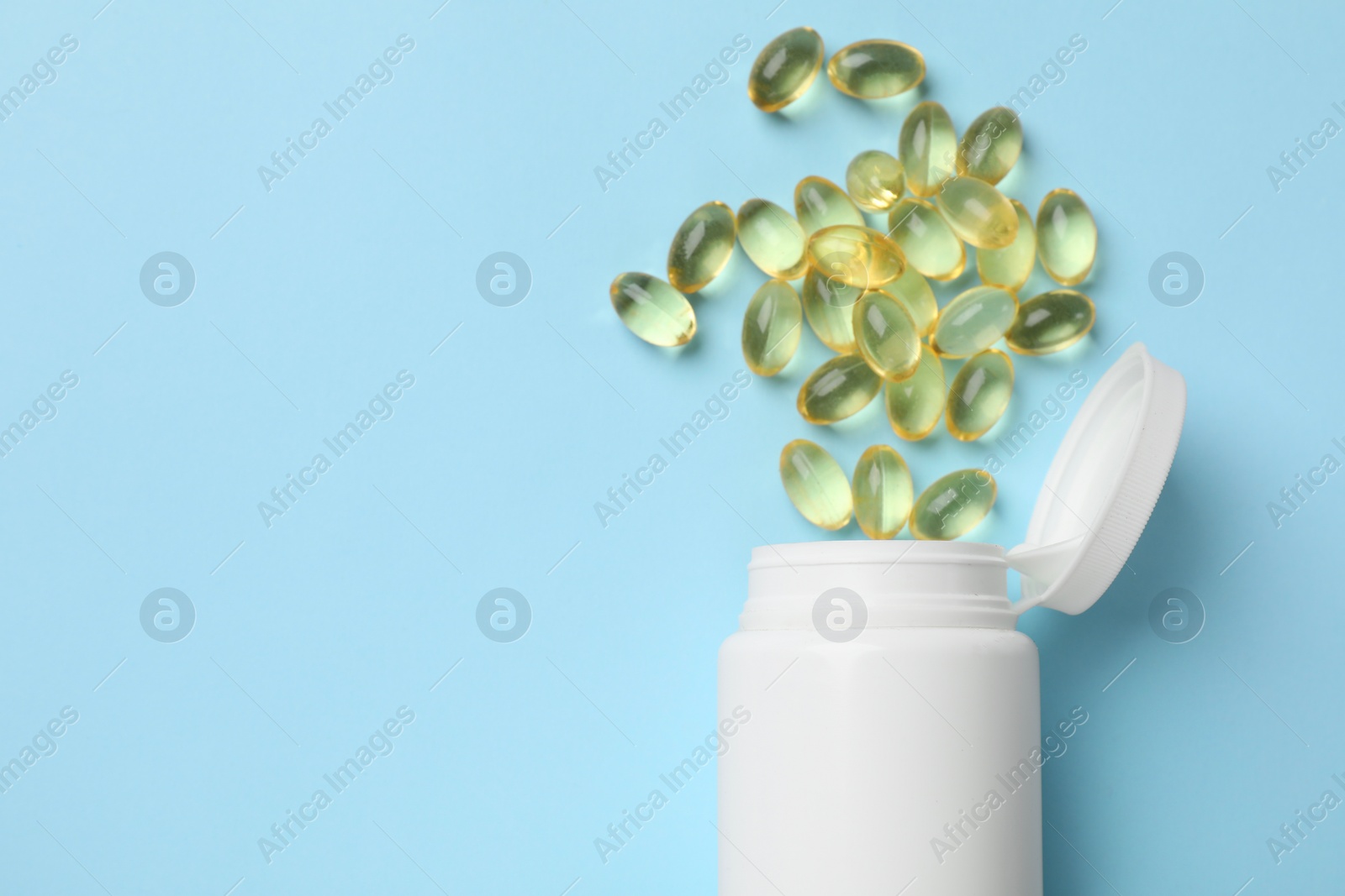 Photo of Vitamin capsules and bottle on light blue background, top view. Space for text