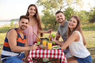 Happy young people having picnic at table in park