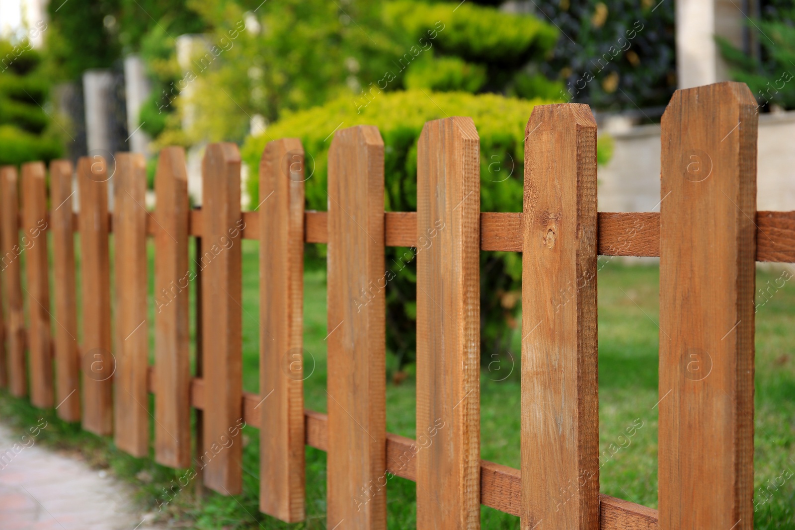 Photo of Closeup view of small wooden fence near green bushes in garden