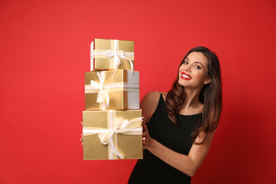 Beautiful woman with Christmas gifts on red background