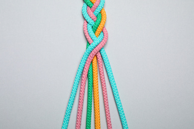 Photo of Braided colorful ropes on light grey background, top view. Unity concept